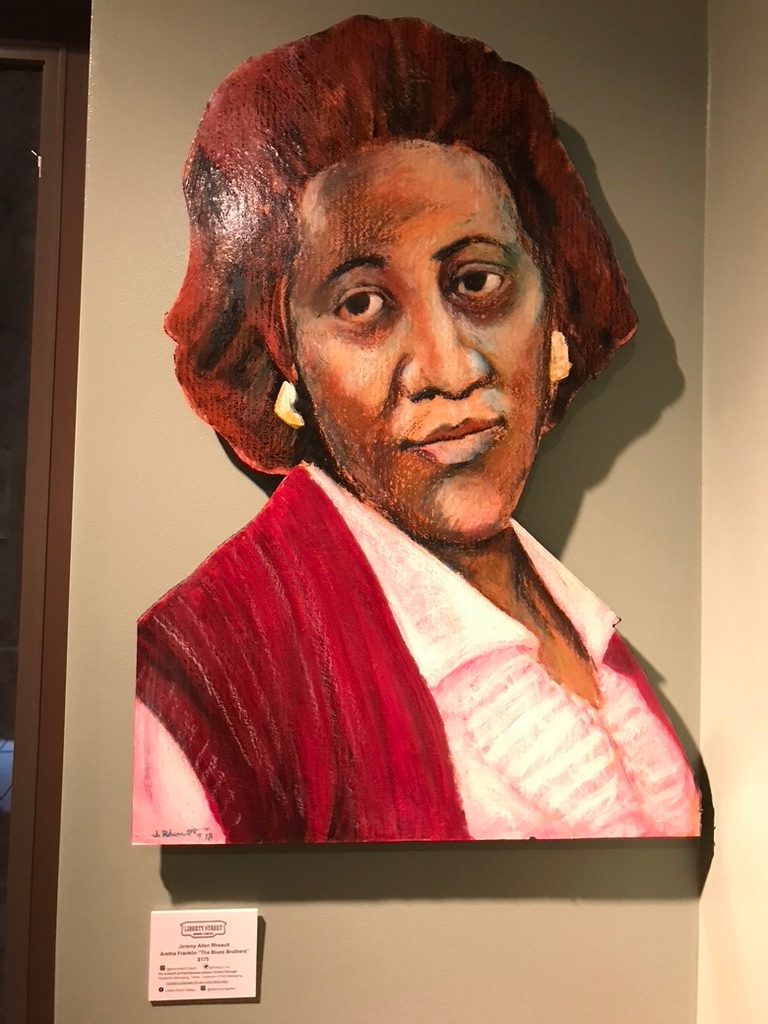 Hand-cut and hand-painted portrait of Aretha Franklin in a red vest and pink collar, on a gallery wall