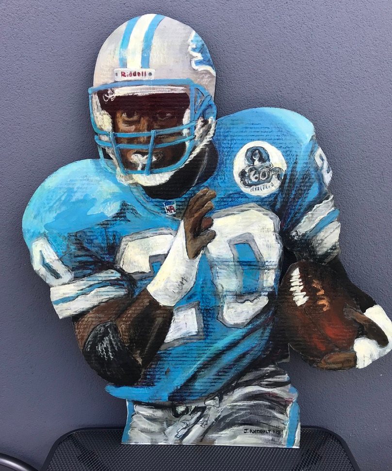 Hand-cut and hand-painted portrait of Barry Sanders in a Detroit Lions helmet and blue jersey, carrying a football, on a gray wall