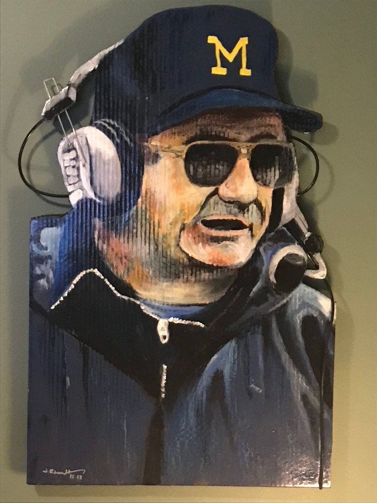 Hand-cut and hand-painted portrait of Bo Schembechler in a Michigan M cap, sunglasses and coaching headset, on a green wall