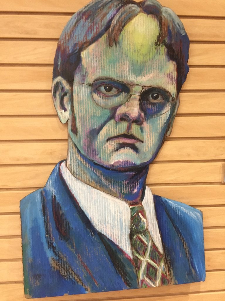 Hand-cut and hand-painted portrait of Dwight Schrute in round glasses, blue suit and patterned tie, on a wood slat wall