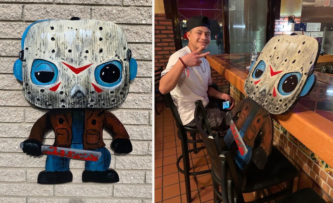 Hand-cut and hand-painted Funko Pop style Jason Voorhees in a cracked hockey mask with blue eyes, a brown jacket and a bloody machete, on a brick wall, and the piece in a restaurant beside the customer