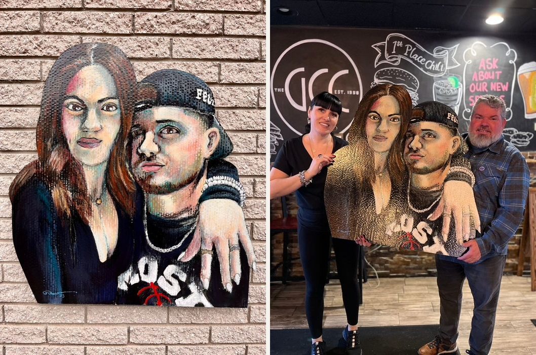 Hand-cut and hand-painted double portrait of a young couple, one in a backwards cap, on a brick wall, and held by two customers in a restaurant
