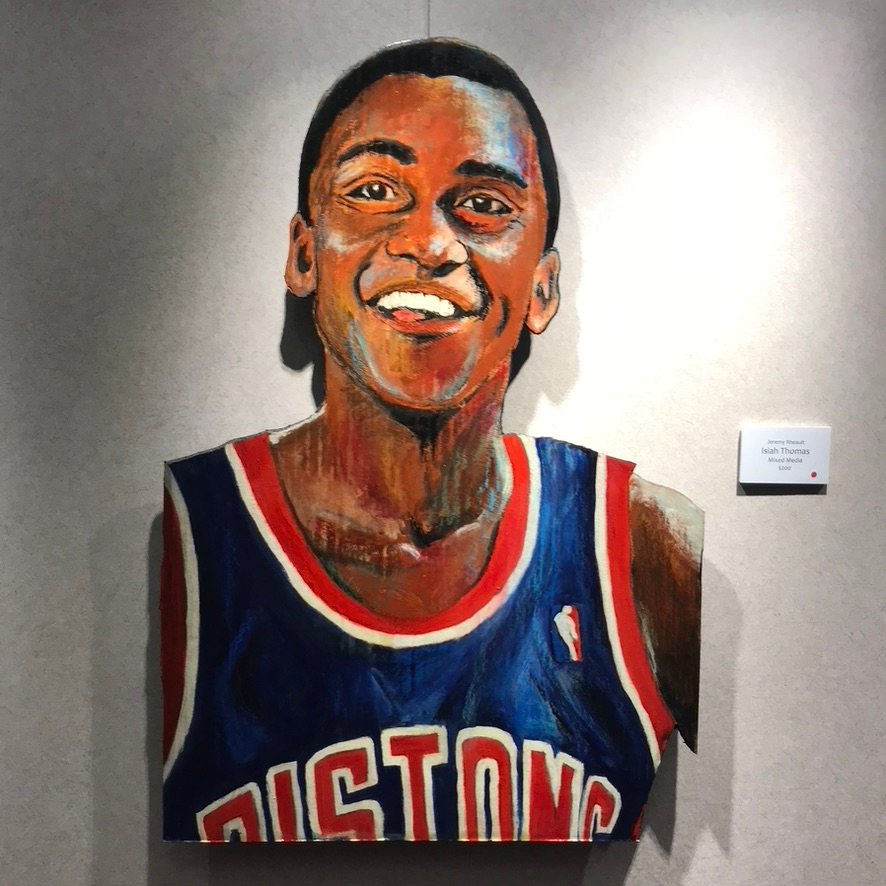 Hand-cut and hand-painted mixed media portrait of Isiah Thomas smiling in a blue Detroit Pistons jersey, on a gallery wall