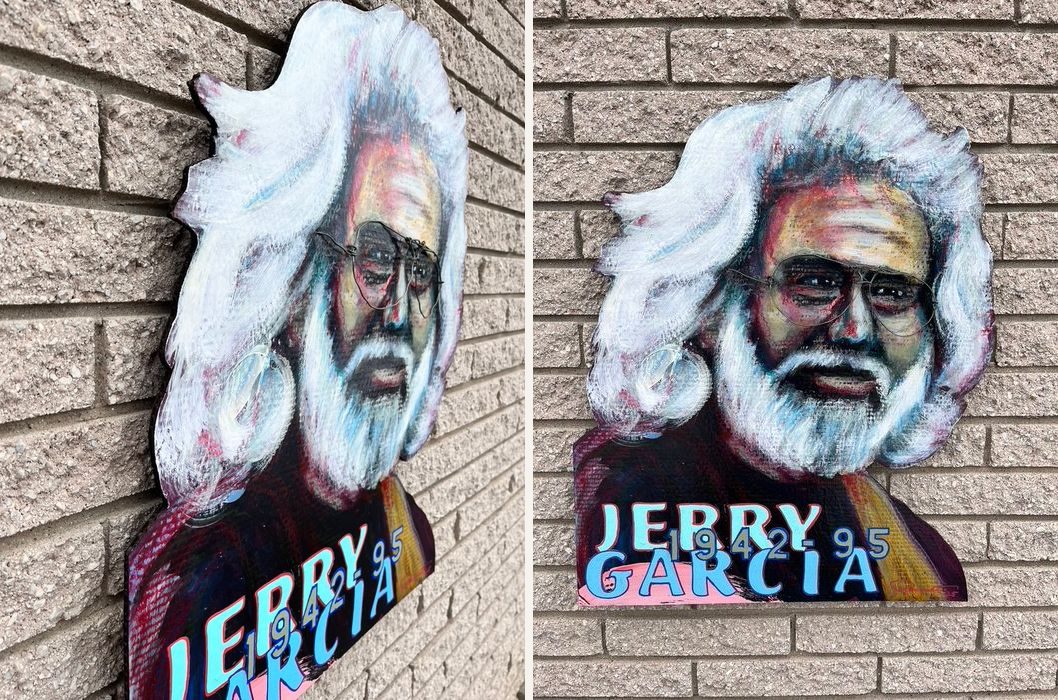 Hand-cut and hand-painted memorial portrait of Jerry Garcia, 1942 to 1995, with white hair and beard and wire glasses, on a brick wall, shown from two photos