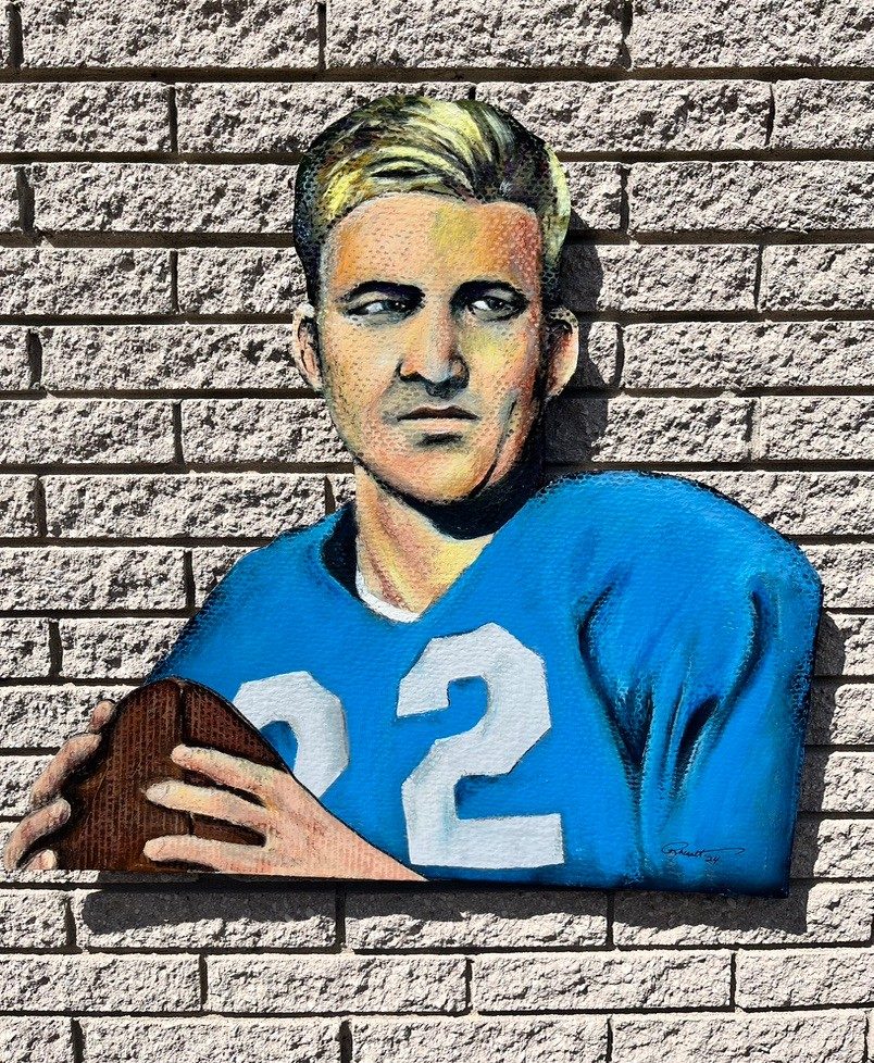 Hand-cut and hand-painted portrait of blond Detroit Lions quarterback Bobby Layne, number 22, in a blue jersey holding a football, on a brick wall