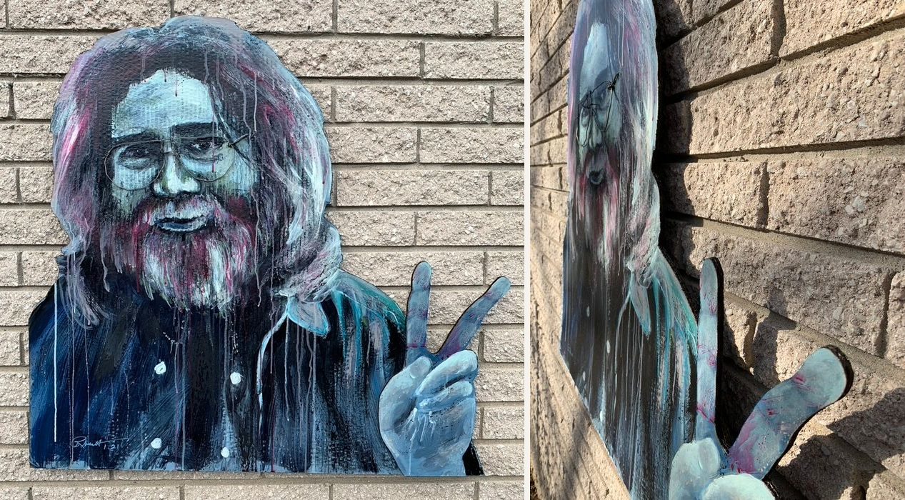 Hand-cut and hand-painted portrait of Jerry Garcia in wire glasses holding up a peace sign, with painted drips: front view on a brick wall and an angled side view showing the layered hand